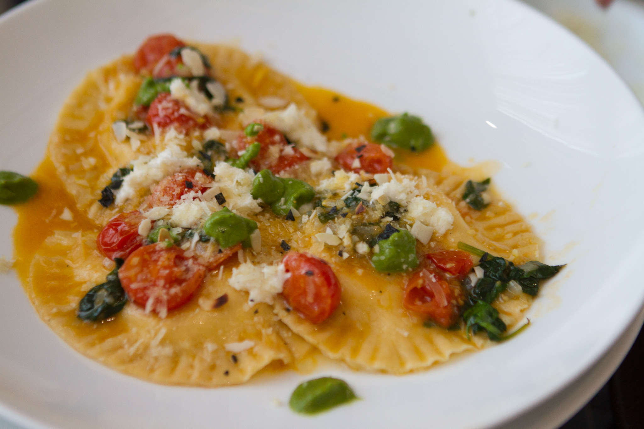 Farfurie cu ravioli în sos de roșii, cu frunze de busuioc și parmezan ras deasupra