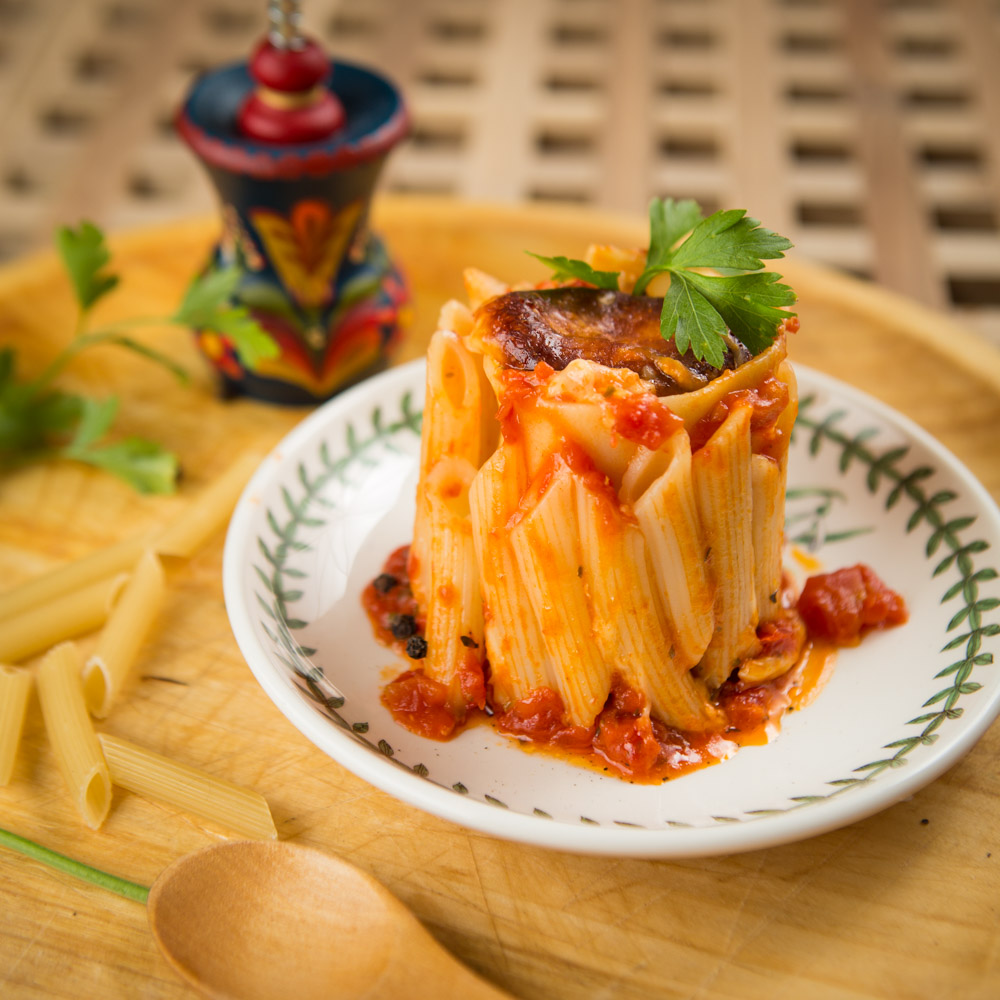 Ruladă de penne cu sos de roșii, servită în picioare pe o farfurie cu model verde