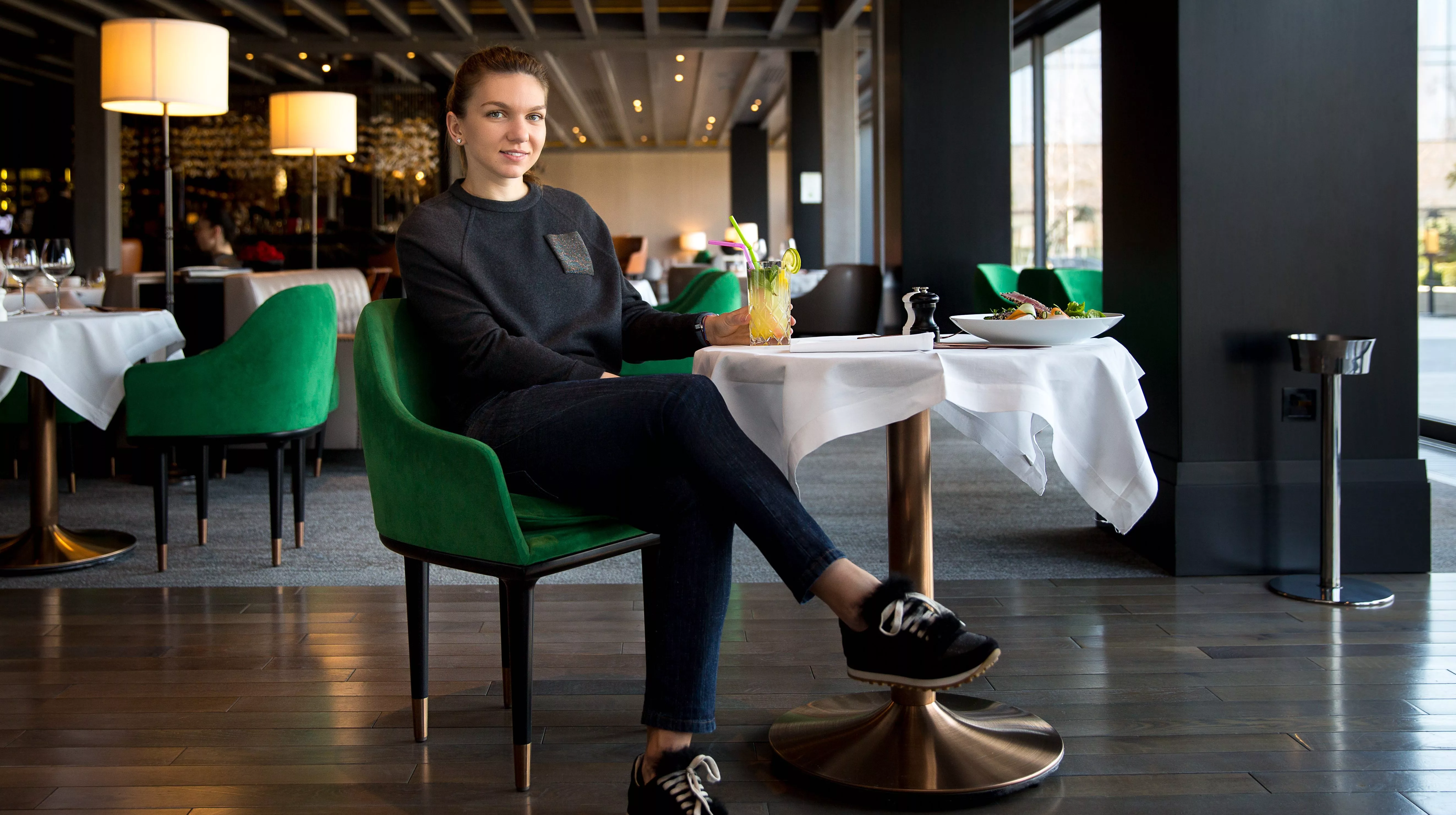 Simona Halep pe un fotoliu verde lângă fereastra restaurantului Stejarii, cadru larg din ședința pentru revista clubului