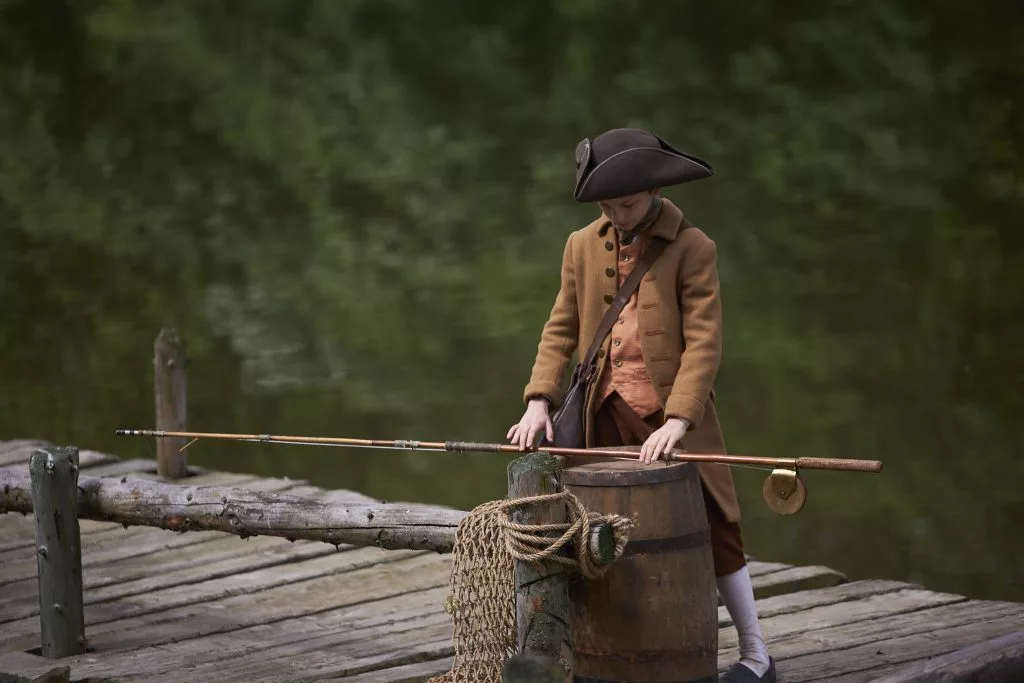 Actor cu pălărie pe un ponton, lângă un butoi — cadru din reclama First Bank