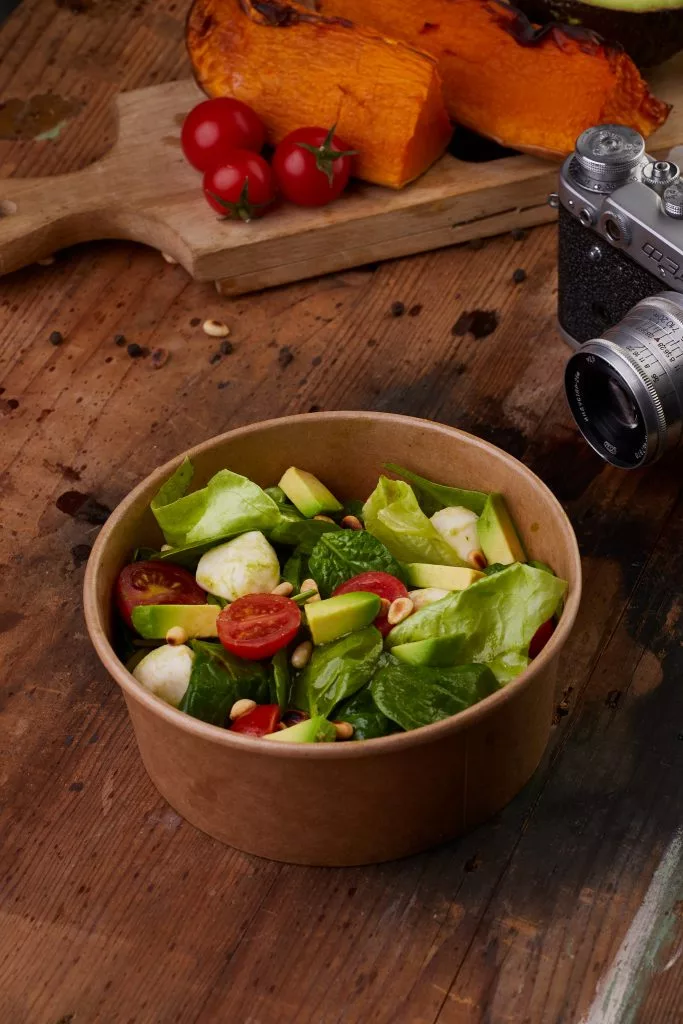 Bol de salată pe masă de lemn, lângă un aparat foto vechi — fotografie culinară Avocadoo