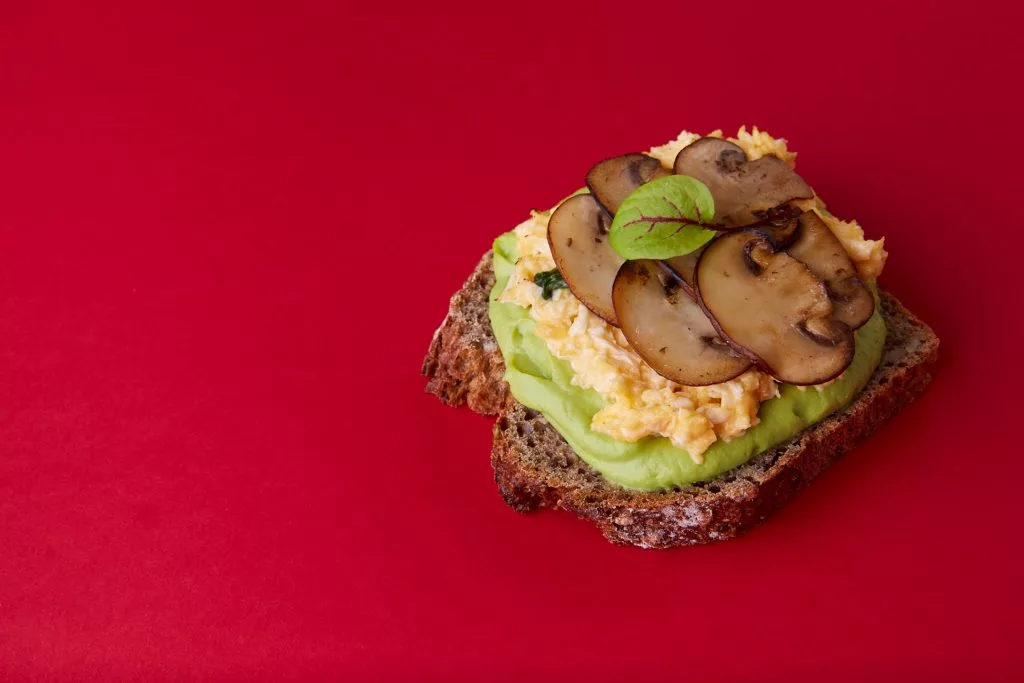 Tartină cu avocado și ciuperci pe fundal roșu, fotografie de produs Avocadoo