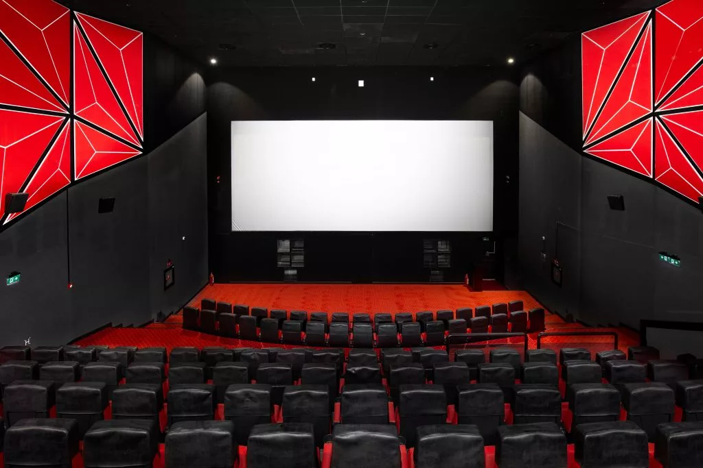 Sala de cinema Cineplex văzută din spate, cu ecranul aprins