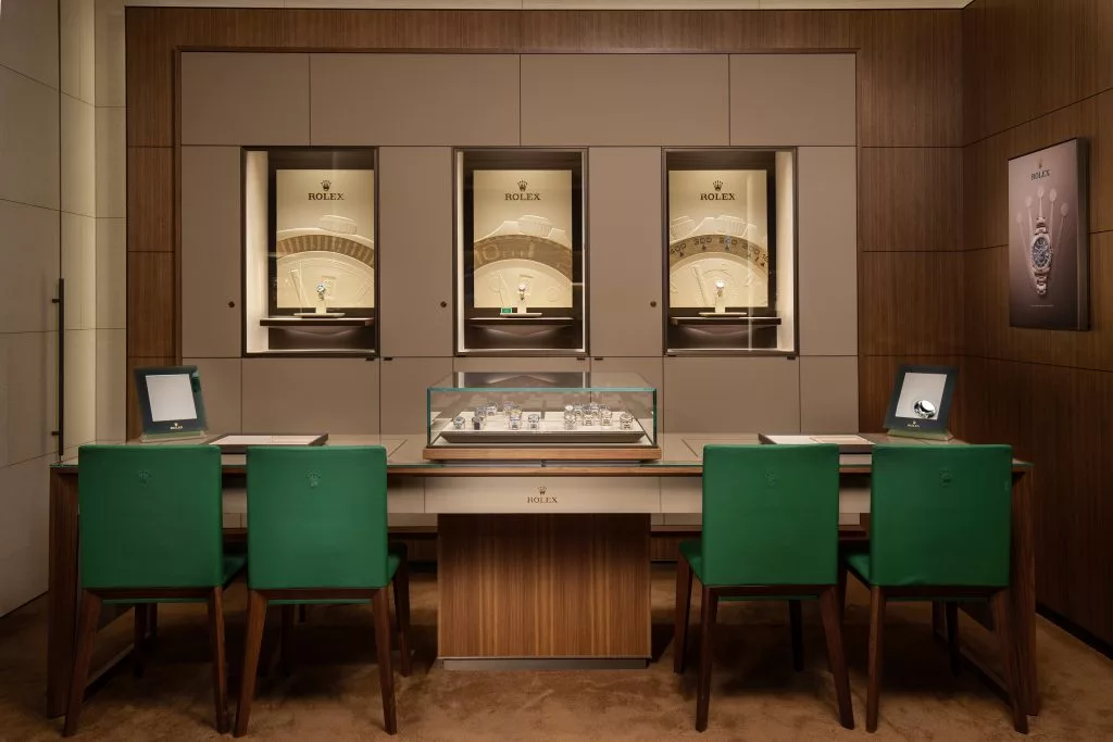 Masă de prezentare cu scaune verzi și vitrine cu ceasuri, magazin ROLEX