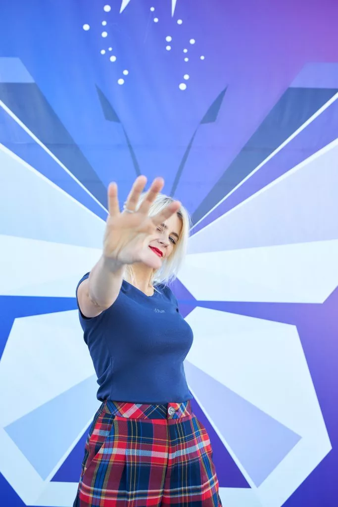 Model cu mâna întinsă spre cameră, pe fundal grafic albastru — campanie s.Oliver