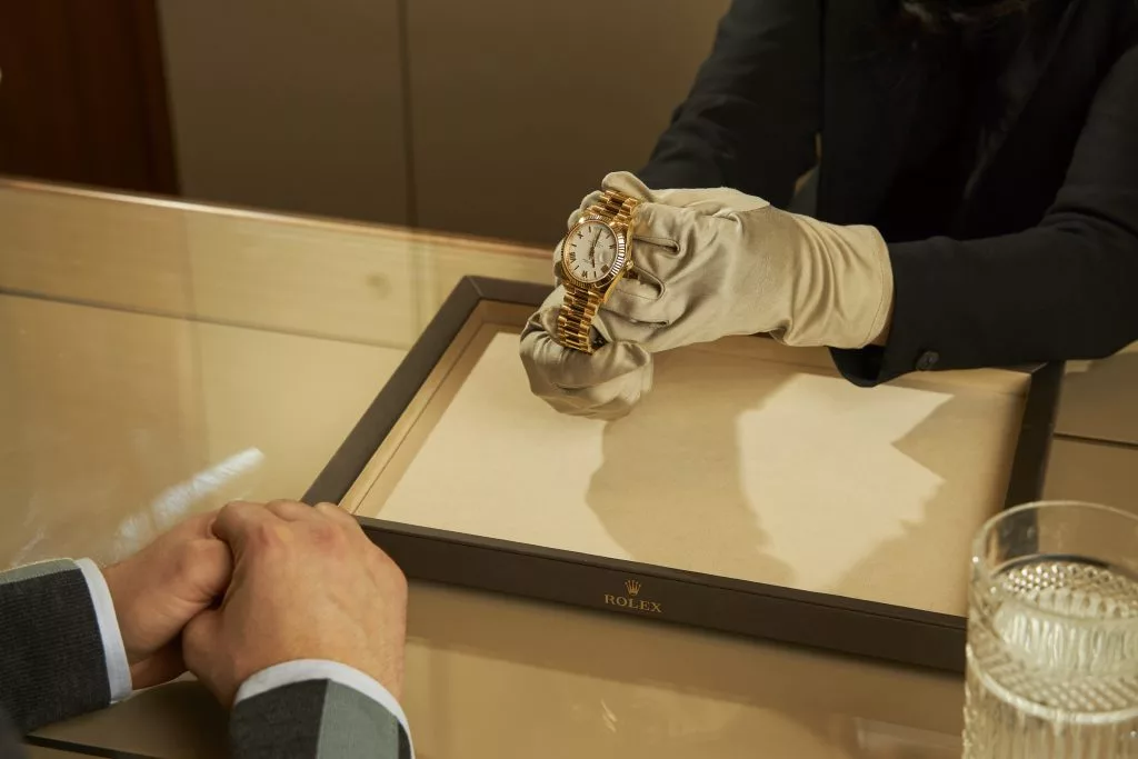 Vânzător cu mănuși albe prezentând un ceas Rolex unui client
