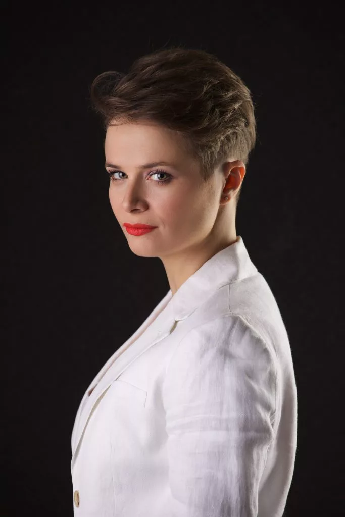 Diana Cavallioti în sacou alb, portret din profil pe fundal negru