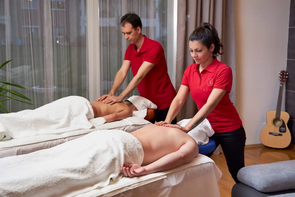 Doi terapeuți KEIGO lucrând simultan asupra unui client, în cabinetul cu chitară pe perete