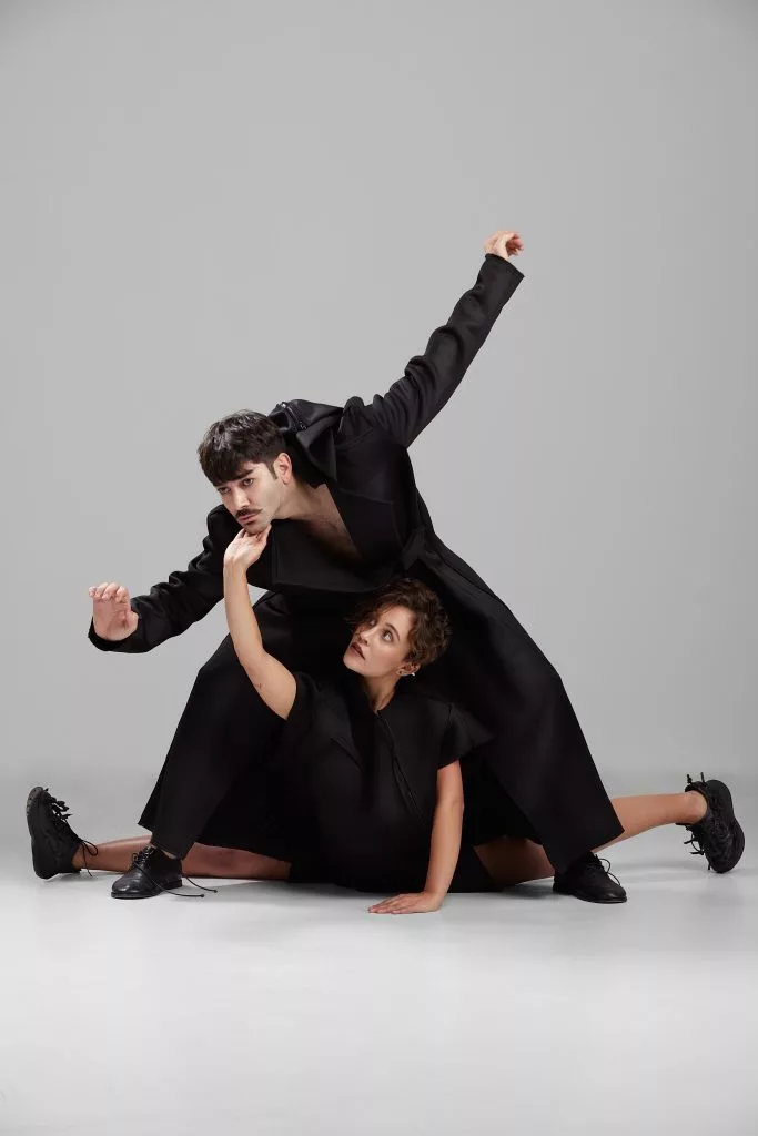 Doi modele în palton negru, într-o figură sprijinită — editorial Fashion Premium Magazine