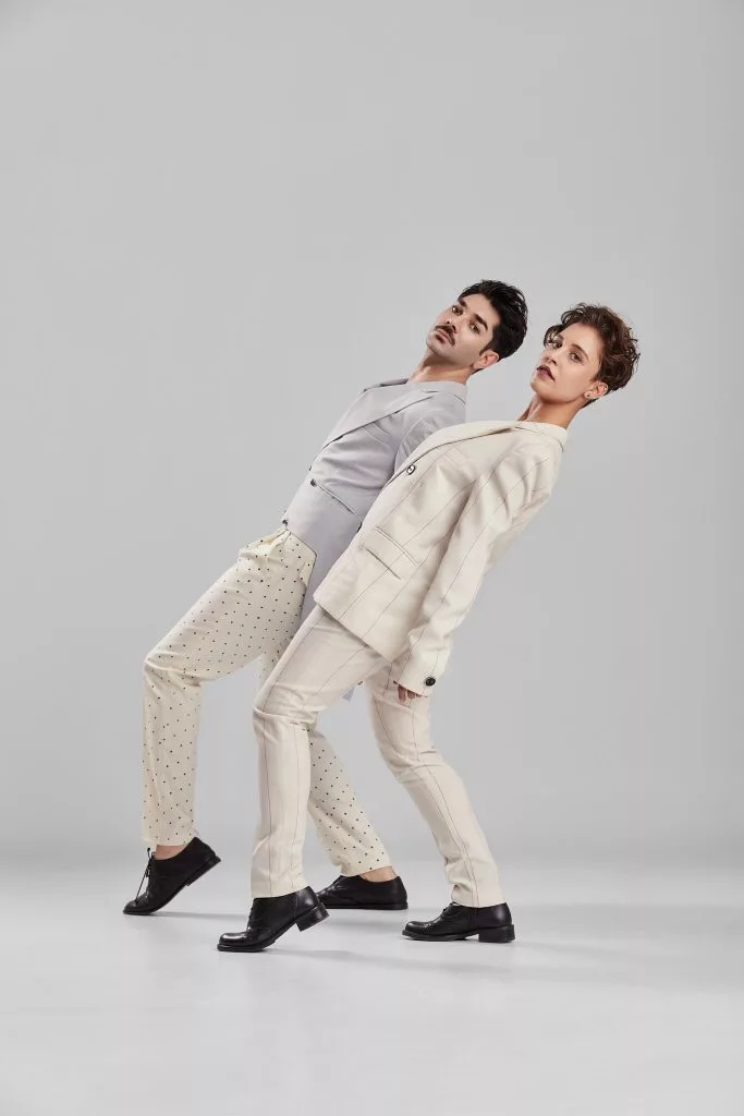 Doi modele în costume bej, înclinați în echilibru — editorial Fashion Premium Magazine