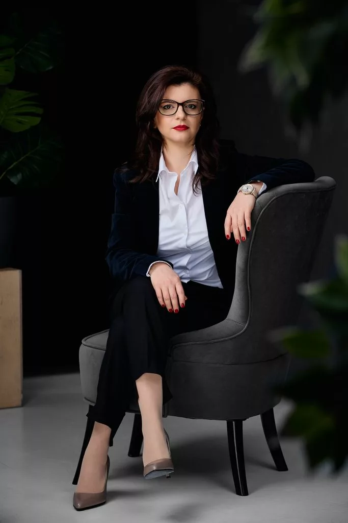 Portret de personal branding: femeie cu ochelari, în costum negru, în fotoliu