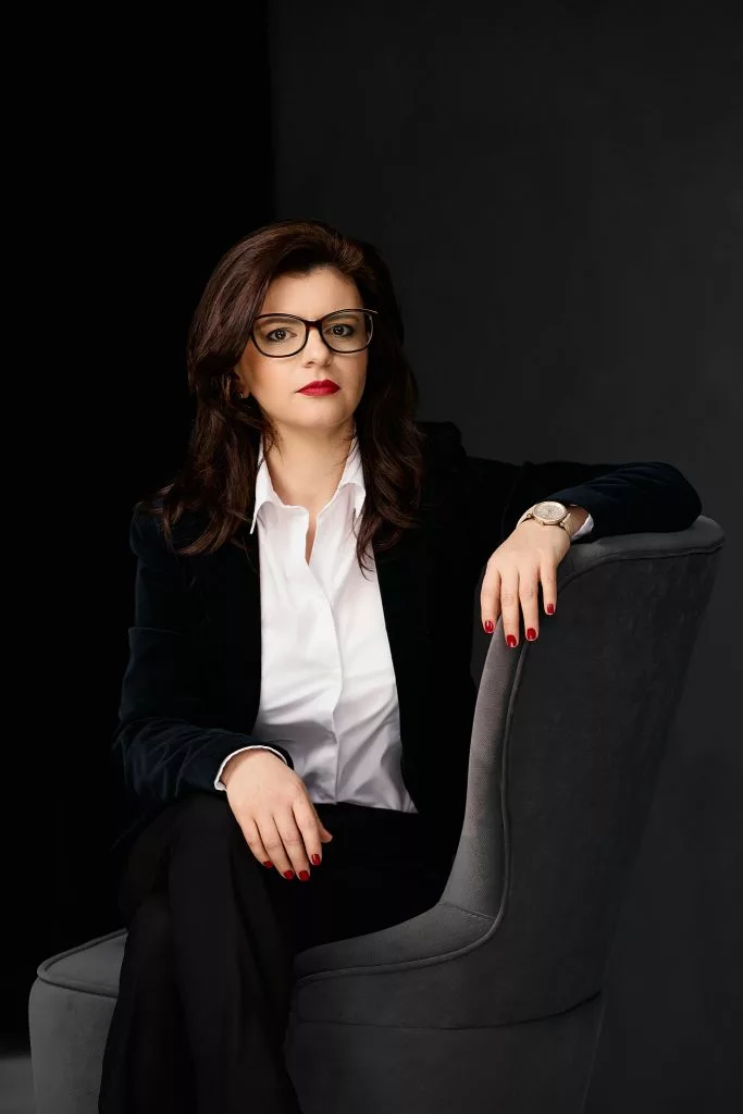 Portret de personal branding: femeie cu ochelari, în sacou de catifea, în fotoliu