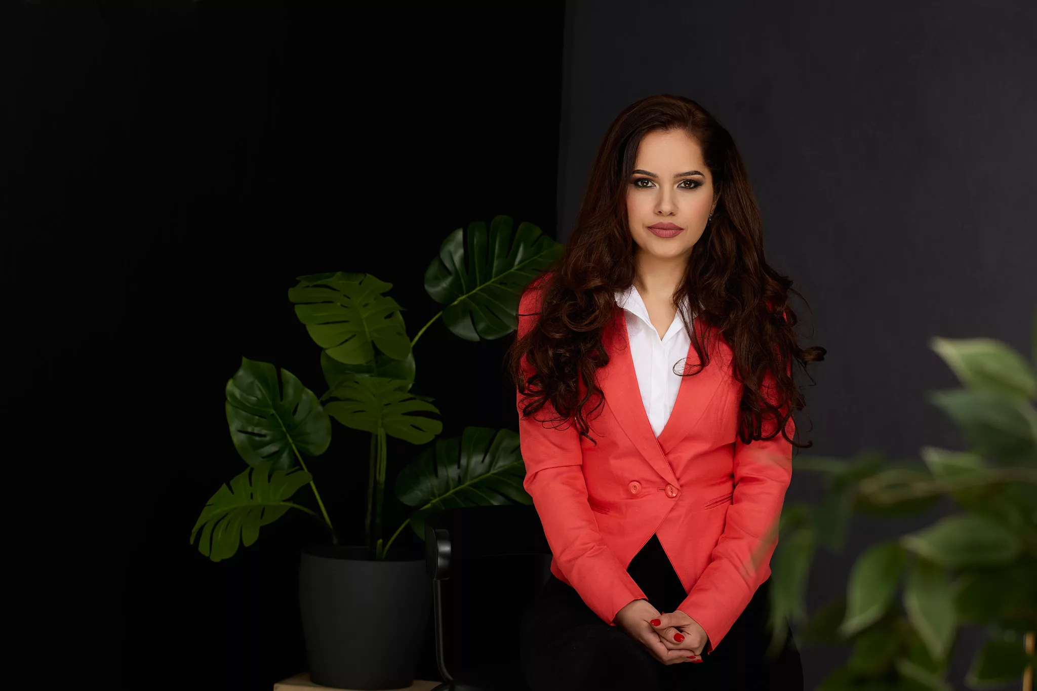 Portret de personal branding: femeie în sacou corai, pe fundal negru cu plante