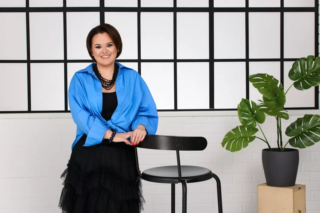 Portret de personal branding: femeie în cardigan albastru, în fața ferestrelor industriale